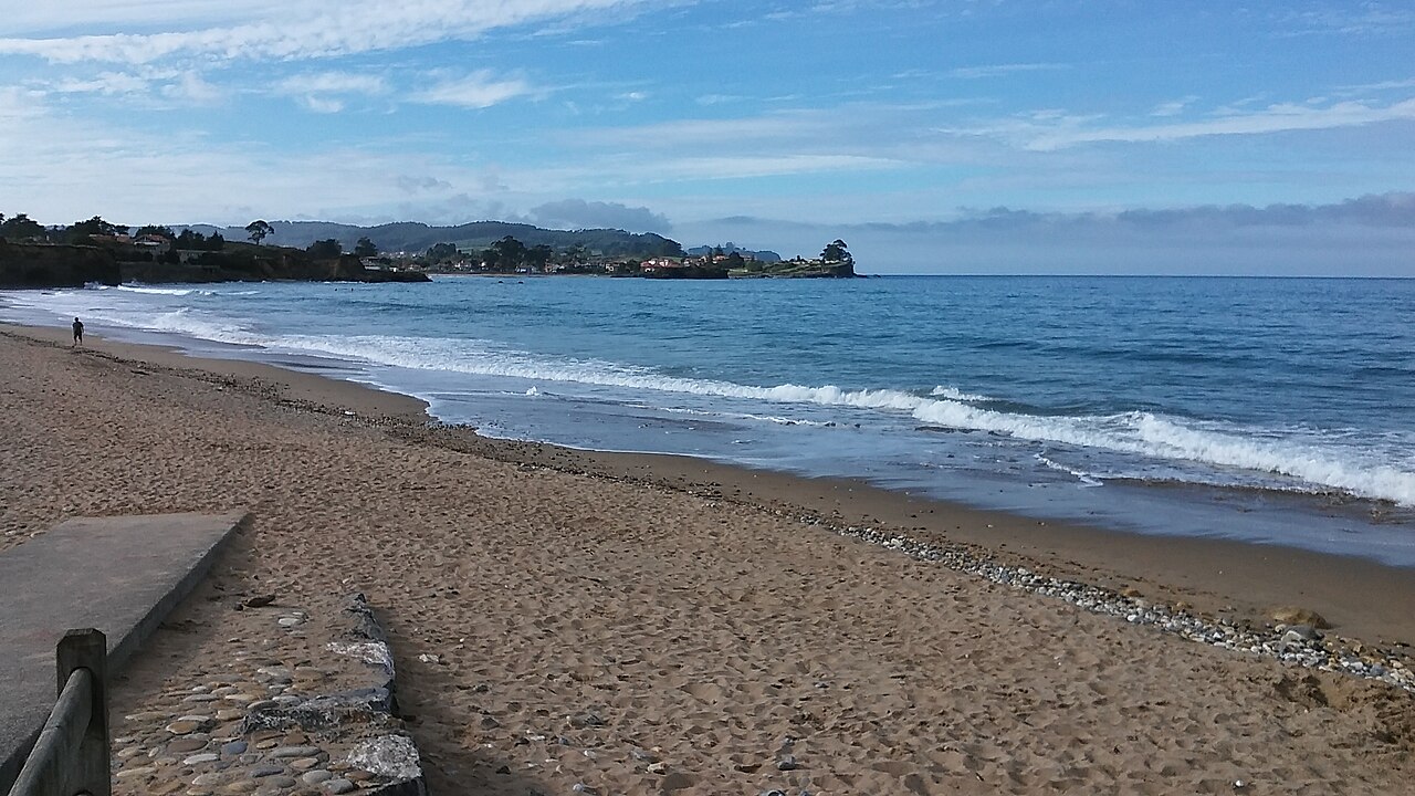 Playa de arena con oleaje y acantilados al fondo en Caravia